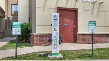 A parking area with a charging station for electric vehicles, a reserved parking sign, and a building with a red door.