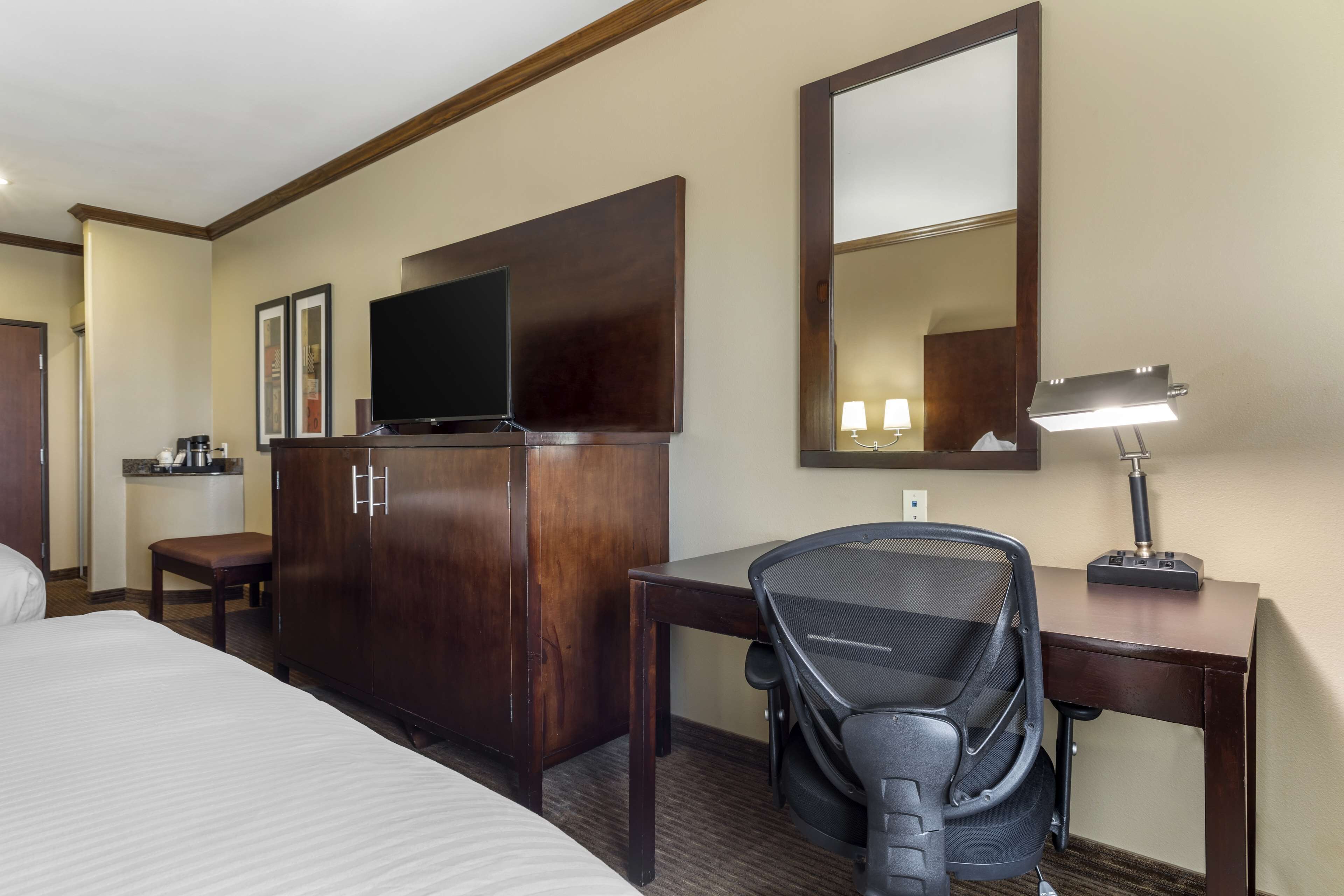 A hotel room with a bed, a desk, a chair, a TV, a wardrobe, and a mirror.
