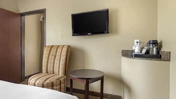 A hotel room with a bed, a patterned armchair, a small table, a television, and a coffee machine.