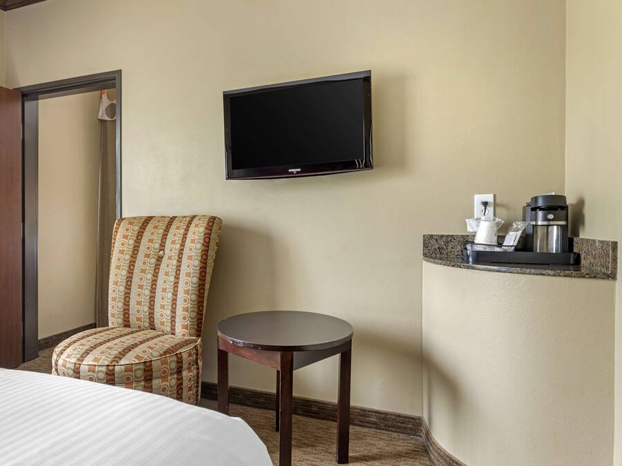 A hotel room with a bed, a patterned armchair, a small table, a television, and a coffee machine.