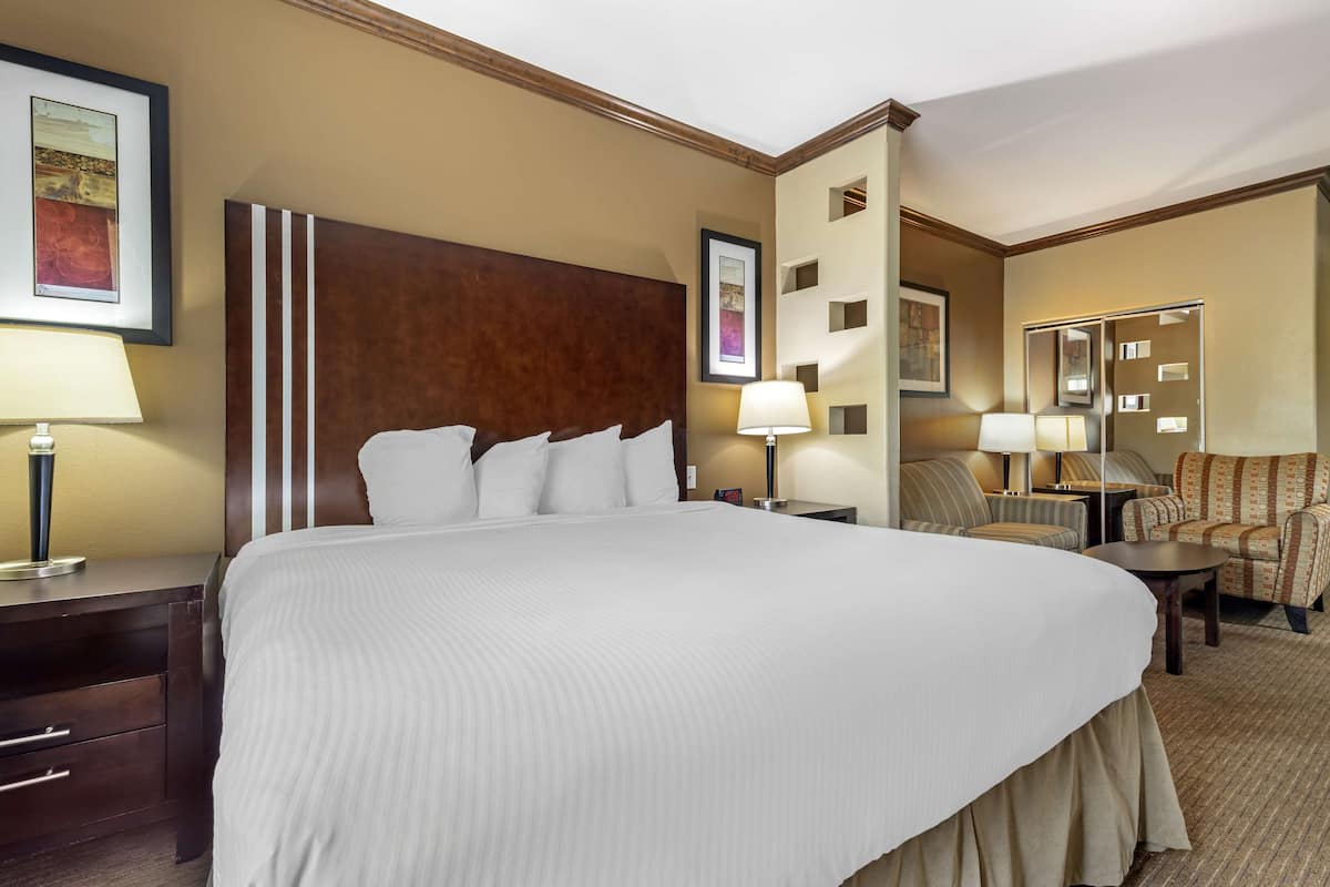 A hotel room with a large bed, two bedside tables with lamps, a chair, and a small table.