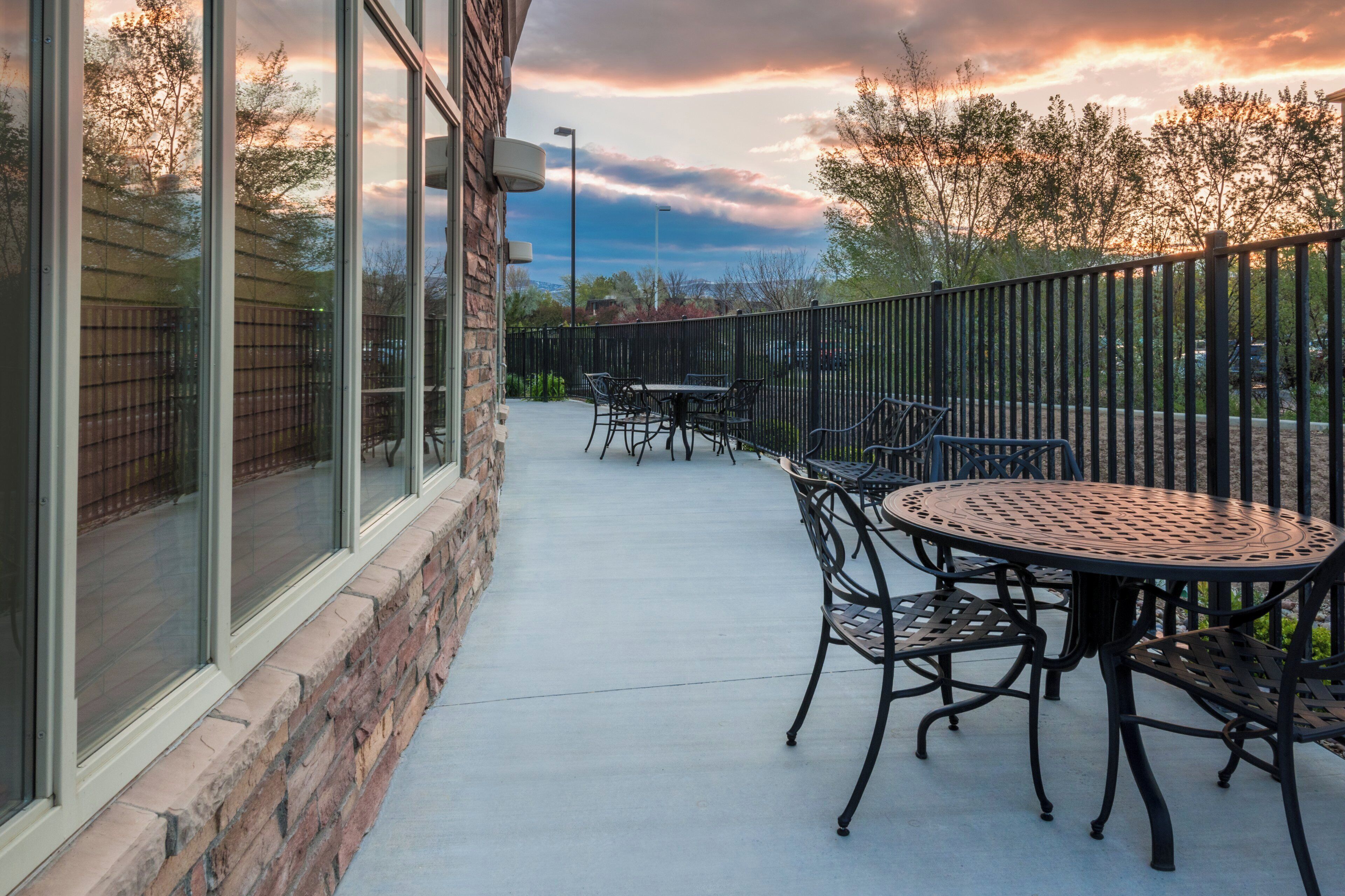 An outdoor patio with tables and chairs, a brick wall, and a view of trees and sky.