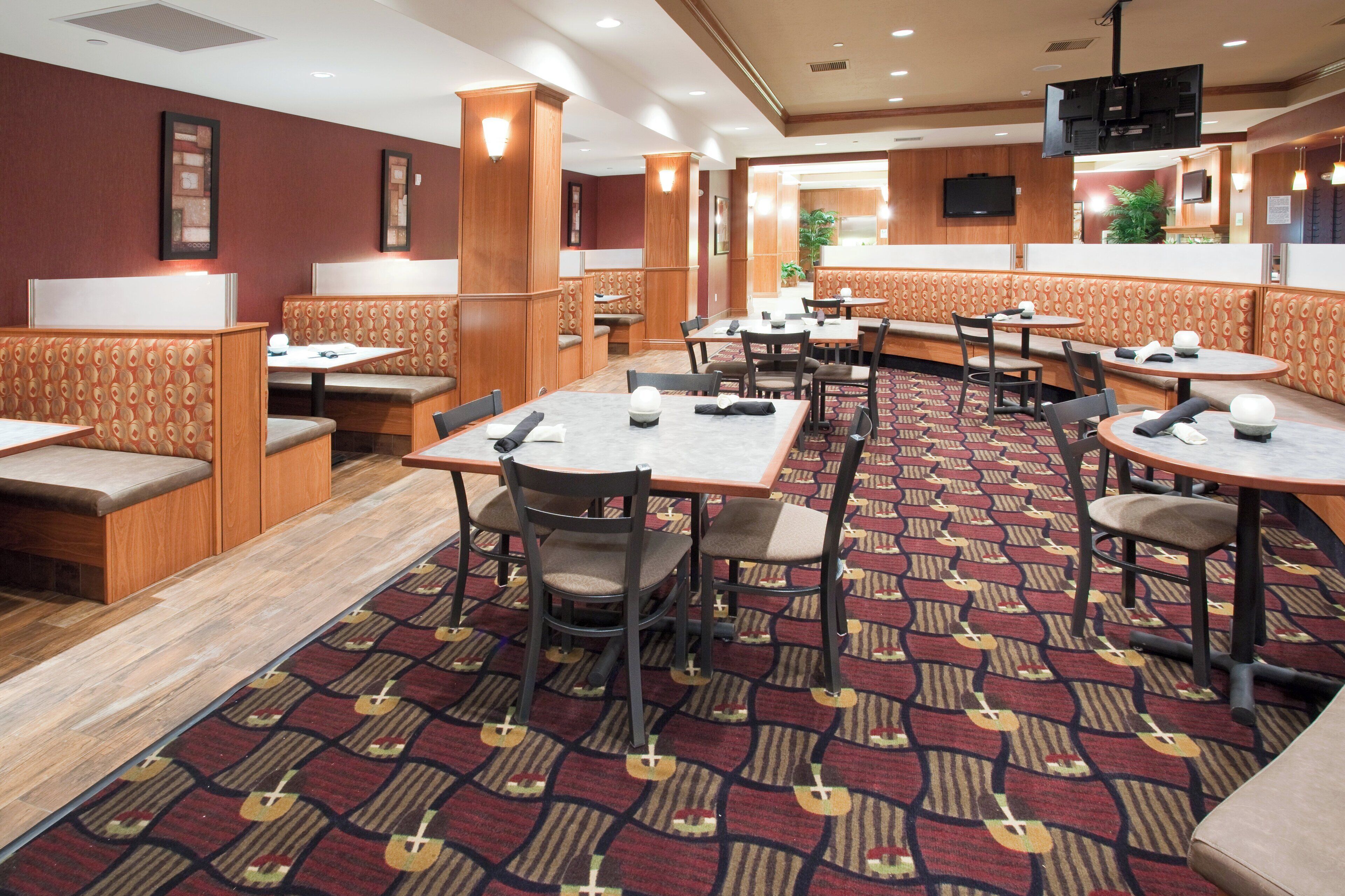 A hotel dining area with booths and tables, carpeted flooring, and wooden paneling.