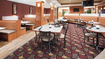 A hotel dining area with booths and tables, carpeted flooring, and wooden paneling.