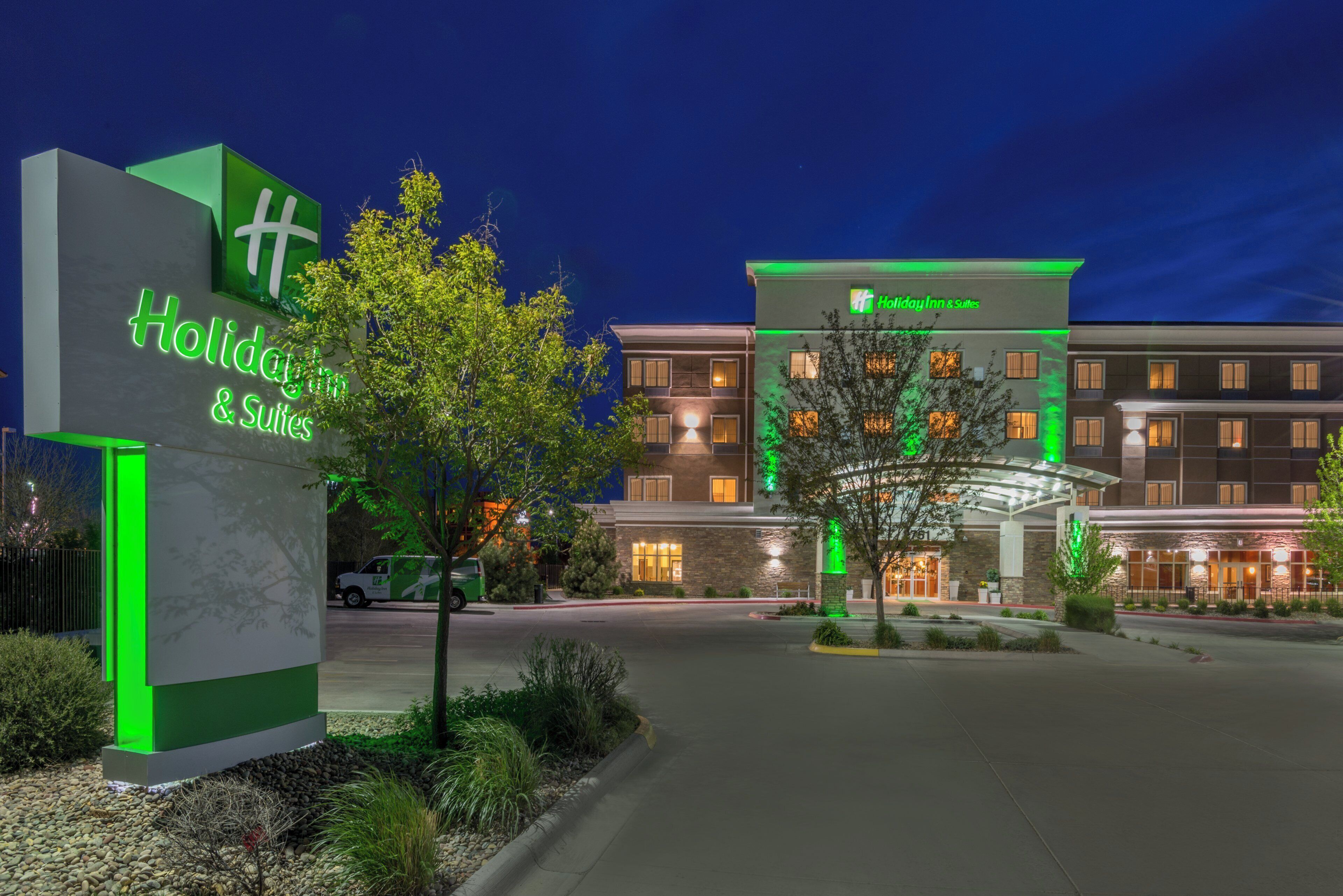 Holiday Inn & Suites -hotelli, jossa on vihreästi valaistu kyltti, katettu sisäänkäynti ja pysäköintialue.