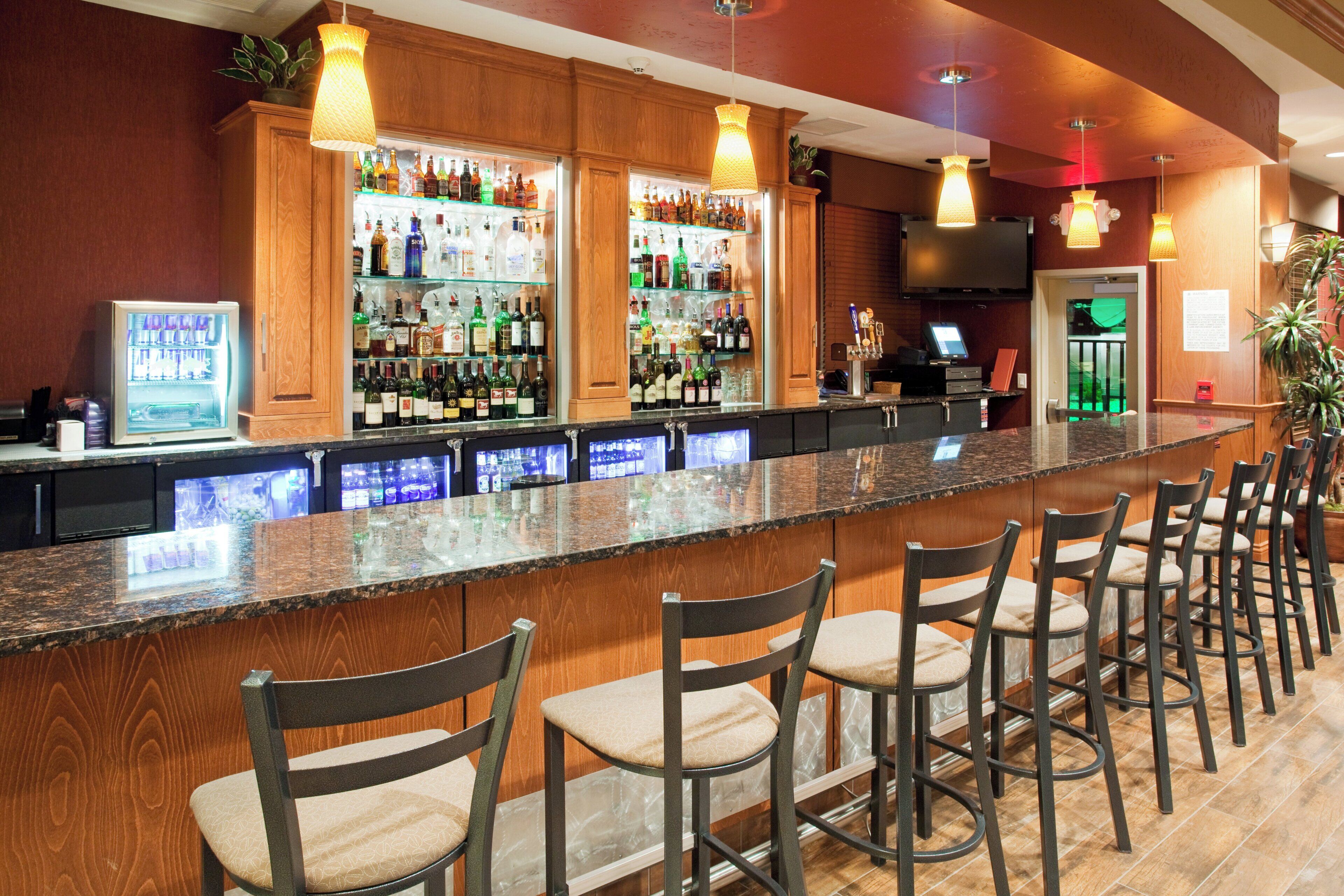 A bar area with a long counter, multiple shelves of liquor bottles, and several bar stools.