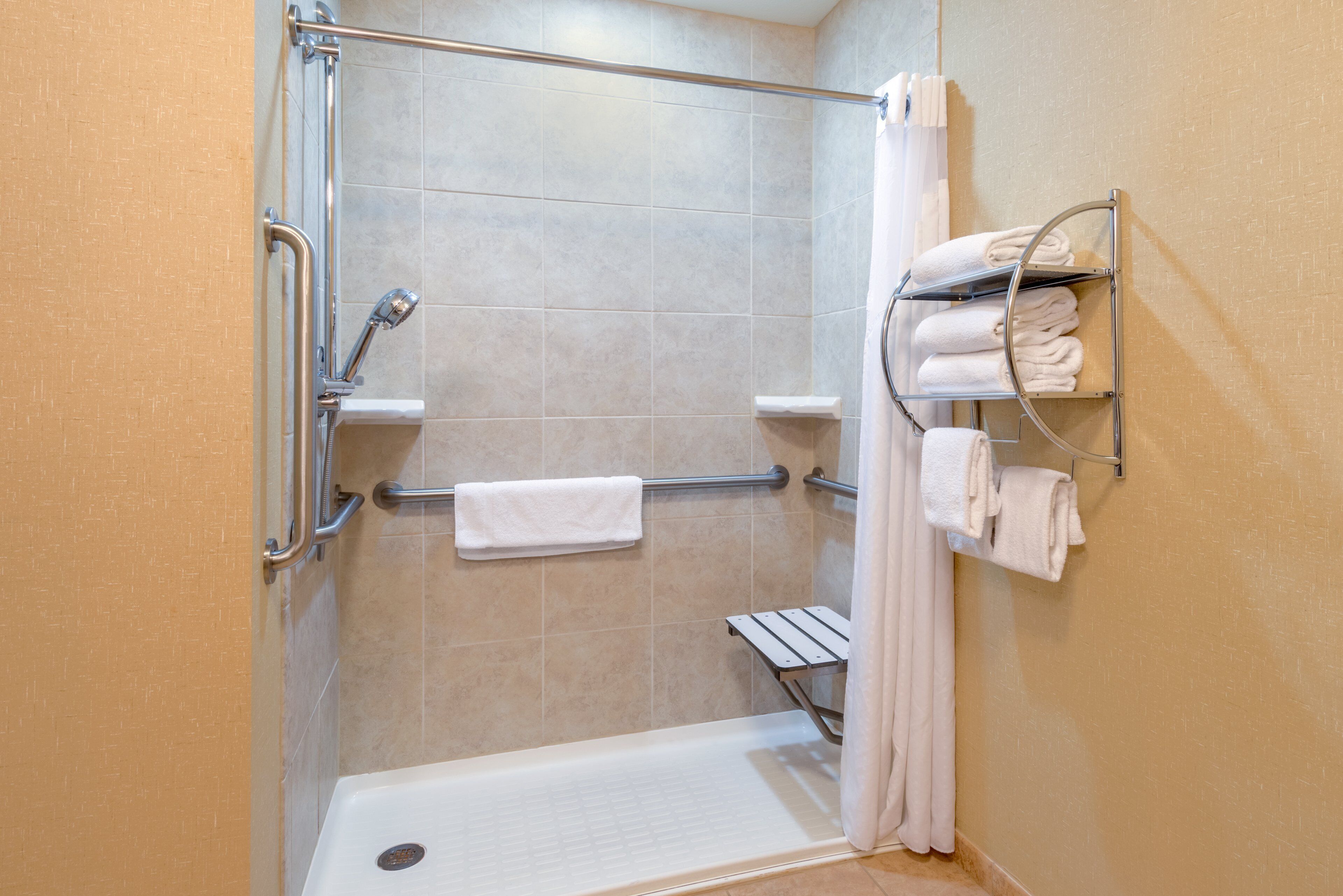 A shower with a grab bar, a white towel rack with towels, and a shower curtain.