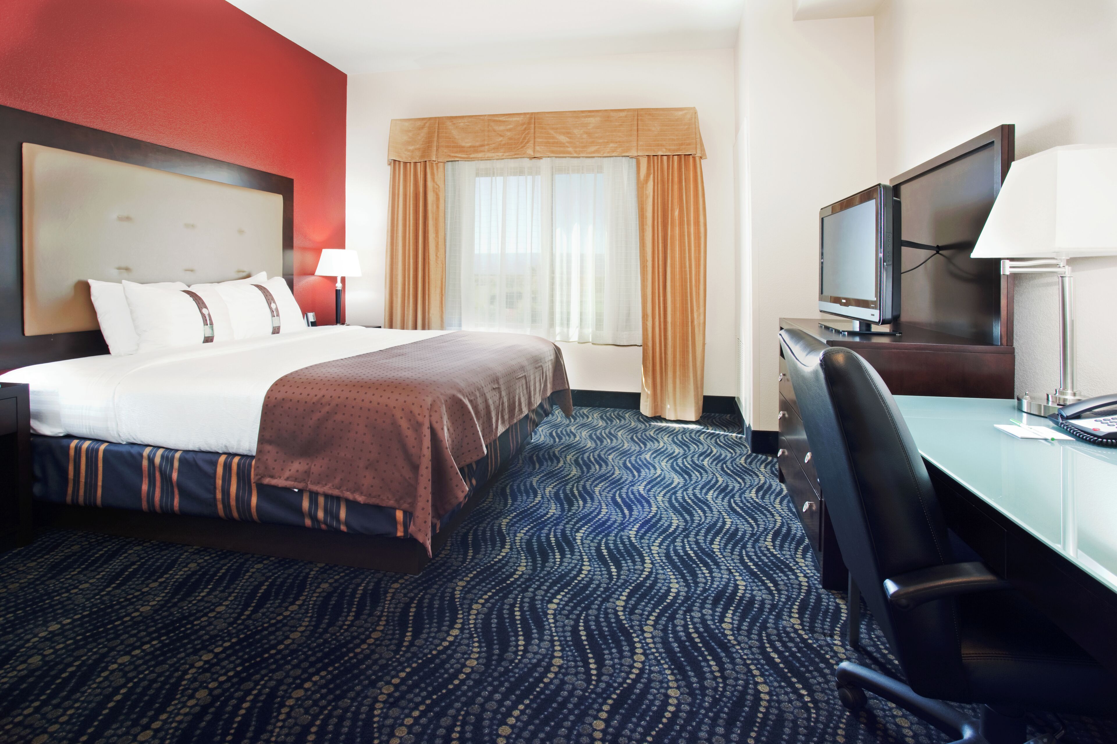 Une chambre d’hôtel avec un lit, un bureau avec une télévision et une chaise.