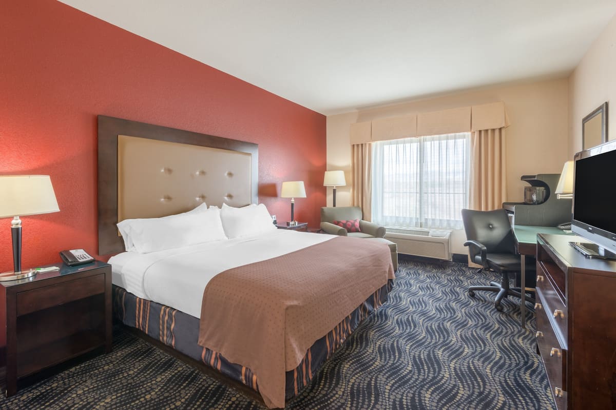 A hotel room with a large bed, a desk with a computer, a chair, a TV, and a window with curtains.