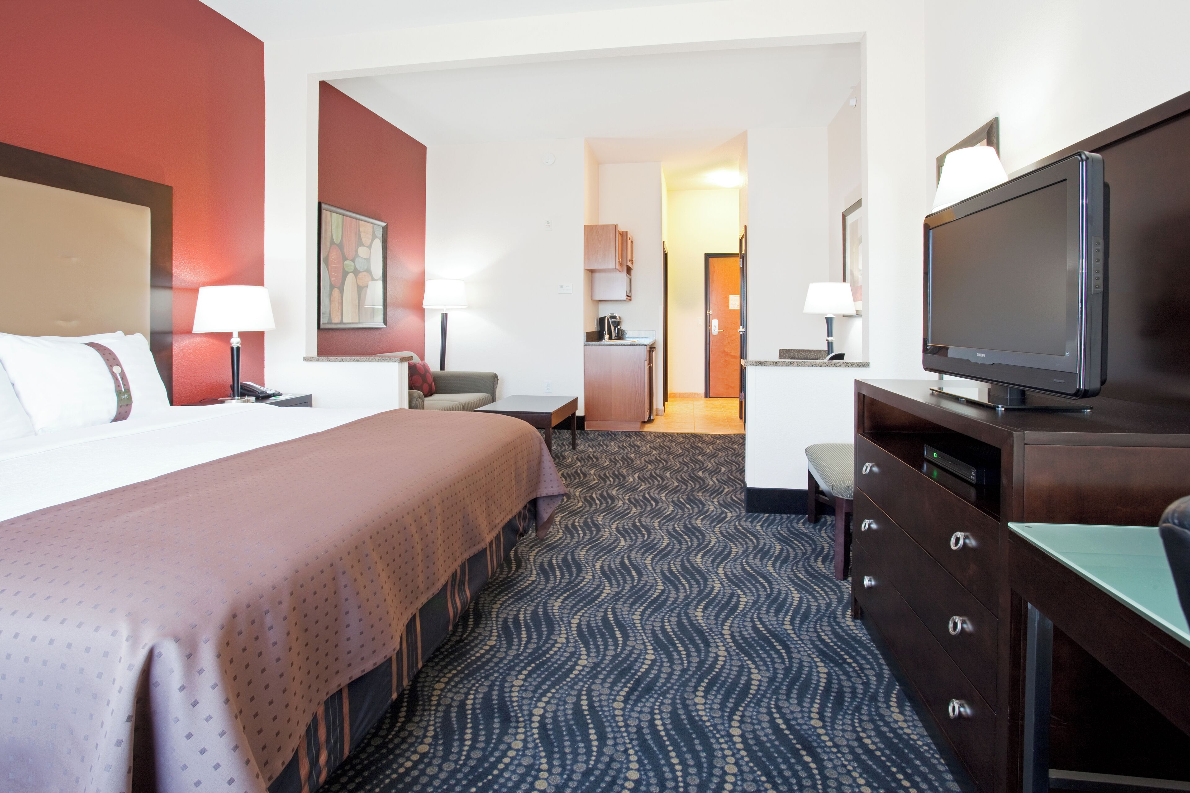 A hotel room with a bed, a desk, a television, and a bathroom visible in the background.