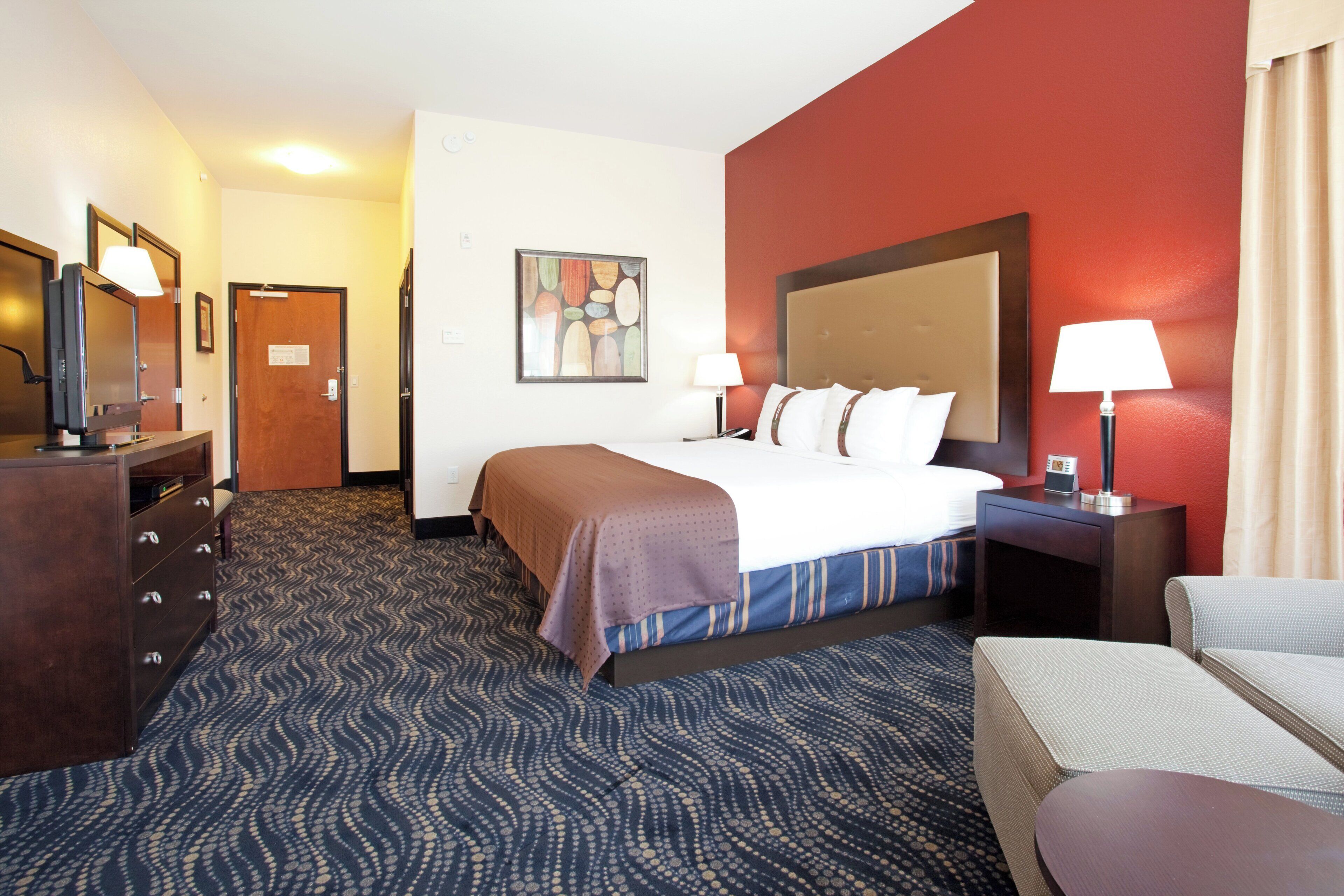A hotel room with a bed, a desk, a chair, a lamp, and a painting on the wall.