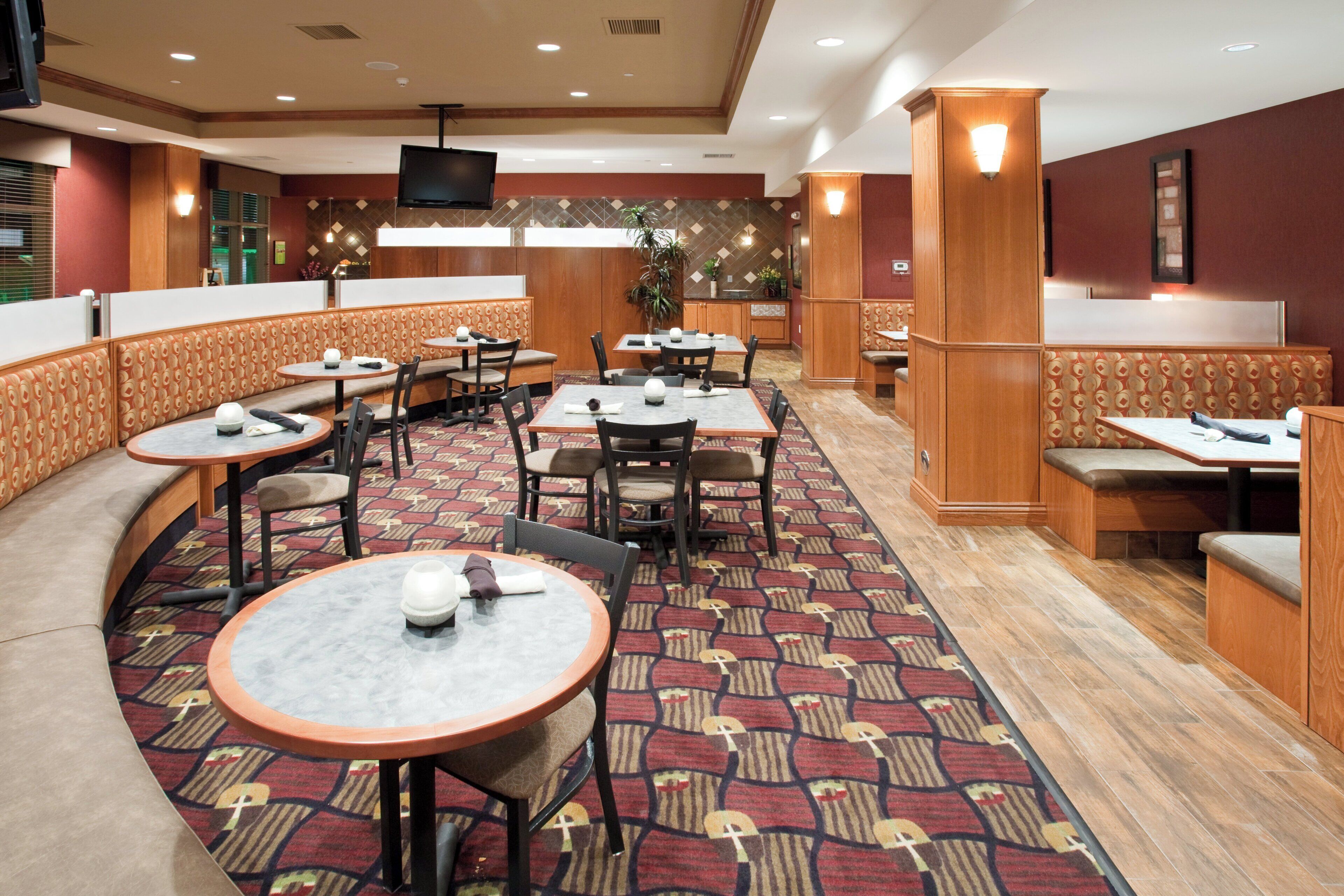 A hotel dining area with round tables, booths, and a television screen.