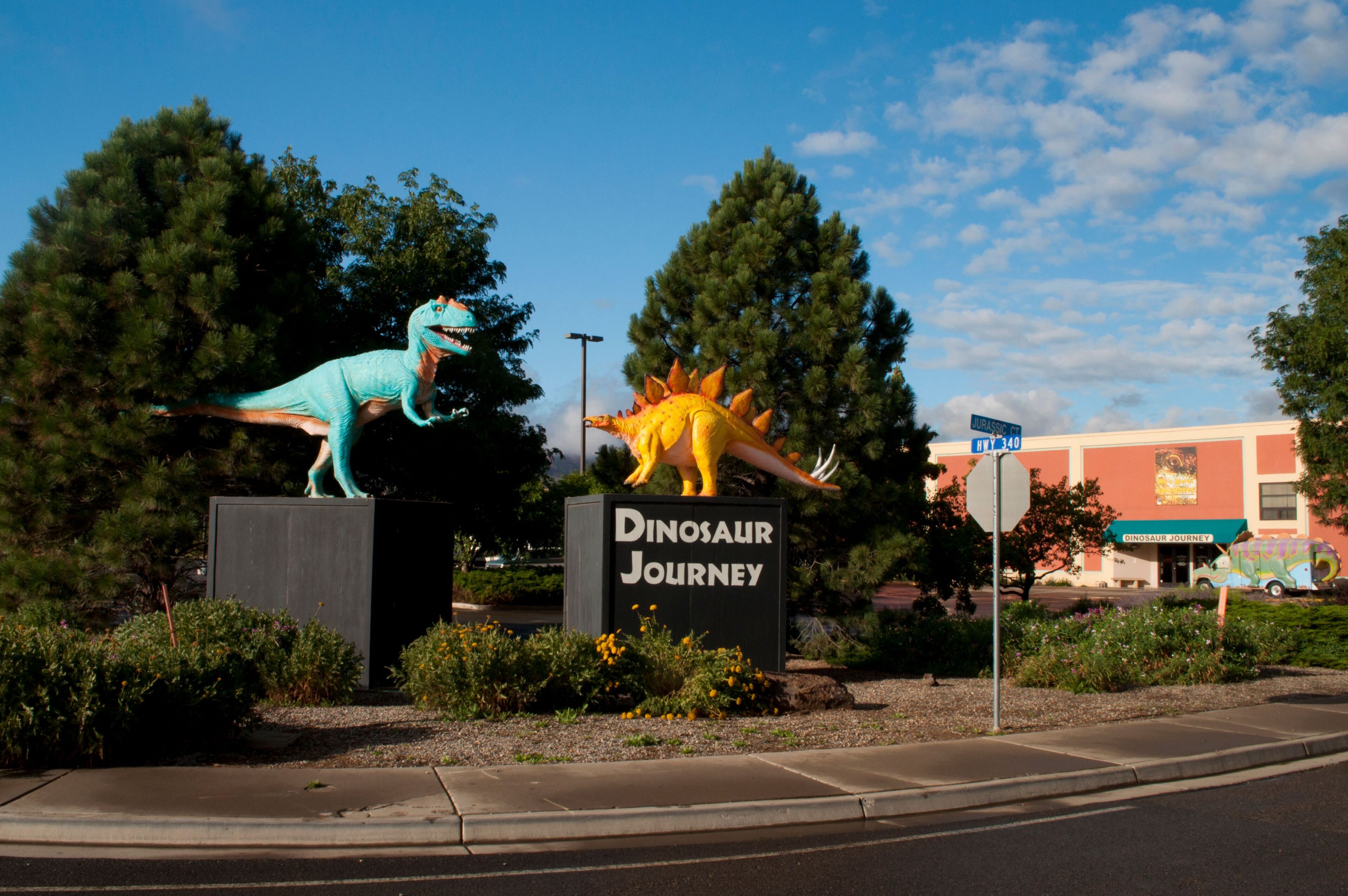 Segnale per 'Dinosaur Journey' con due statue di dinosauri, un edificio sullo sfondo e cielo sereno.