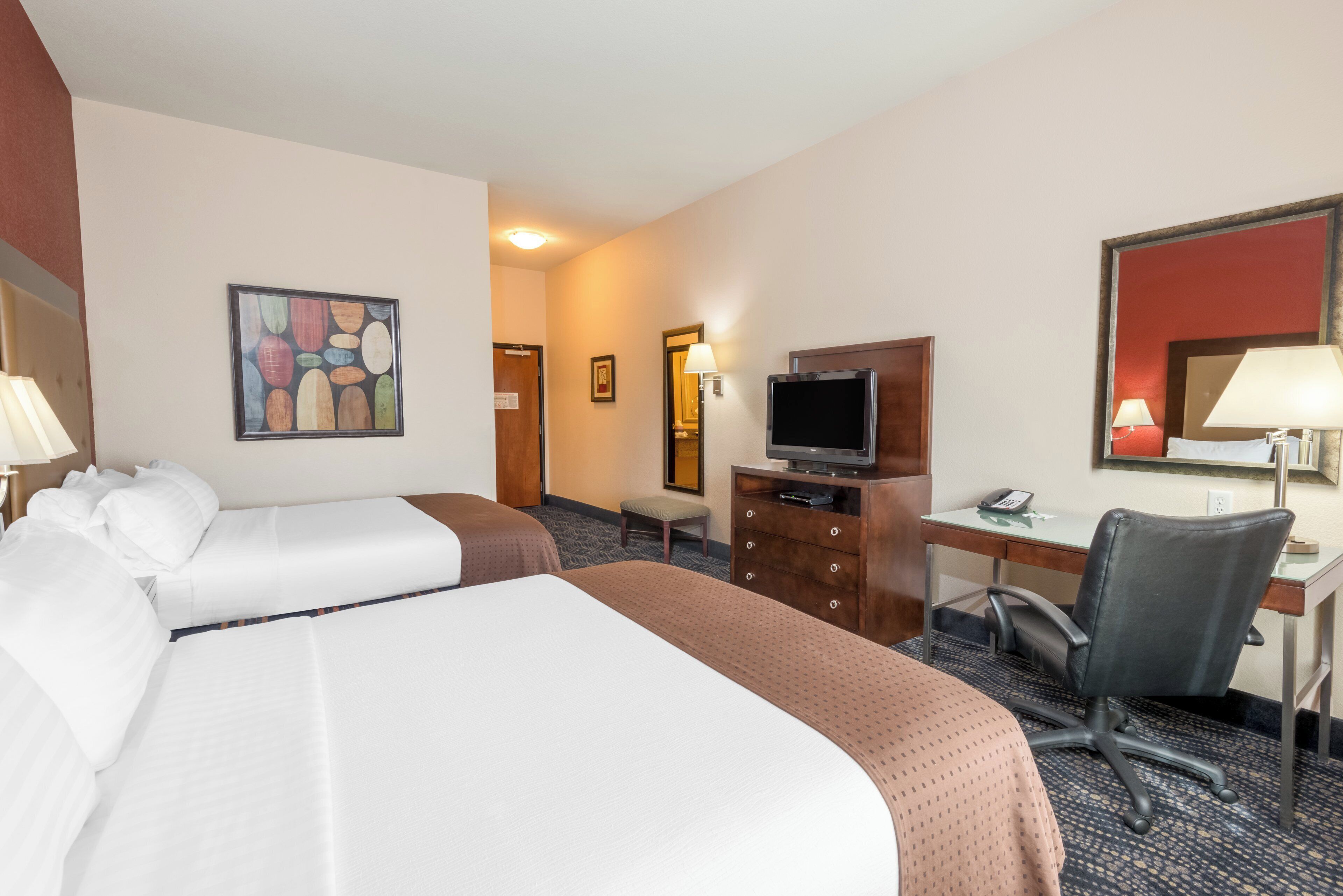 A hotel room with two beds, a desk with a computer, a chair, a television, and a painting on the wall.