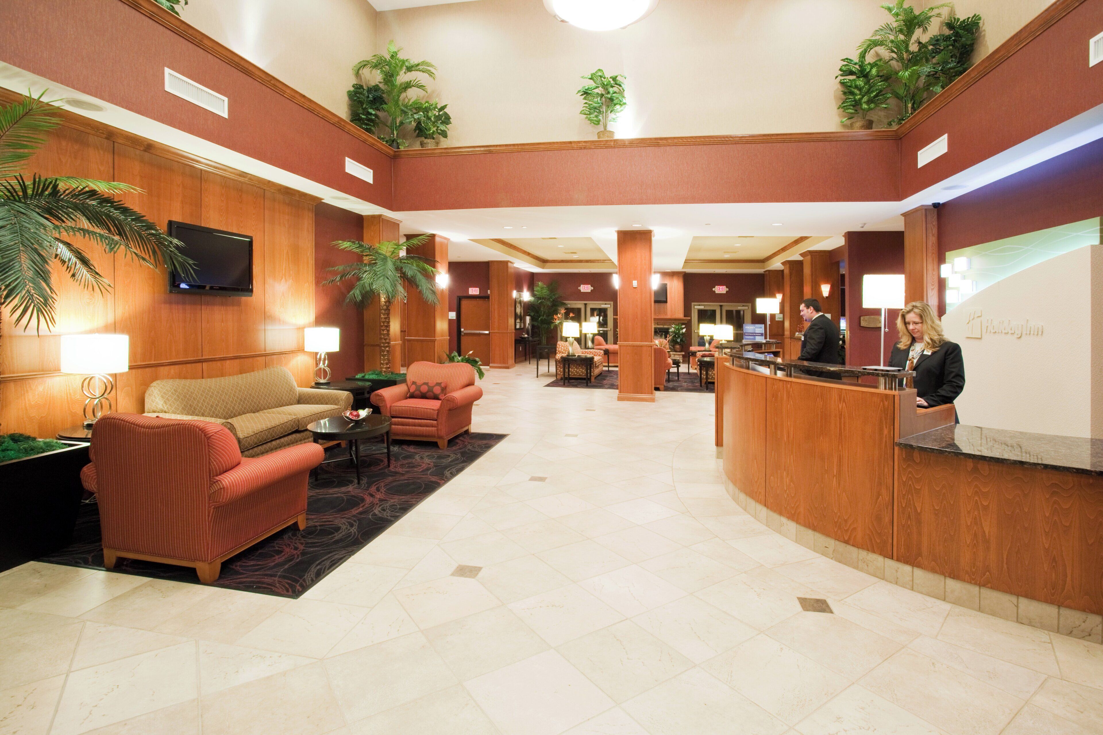 A hotel lobby with a reception desk, seating area, and decorative plants.