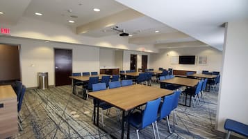 Un salón de conferencias con varias mesas y sillas, un proyector y una pantalla de televisión.