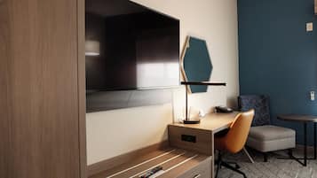 Habitación de hotel con un escritorio de madera, una silla, una lámpara, un televisor y una mesita.