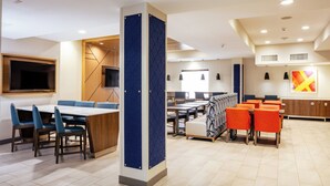 A modern dining area with blue and orange seating, a large table, and a TV mounted on the wall. - Holiday Inn Express & Suites El Paso West by IHG (El Paso)
