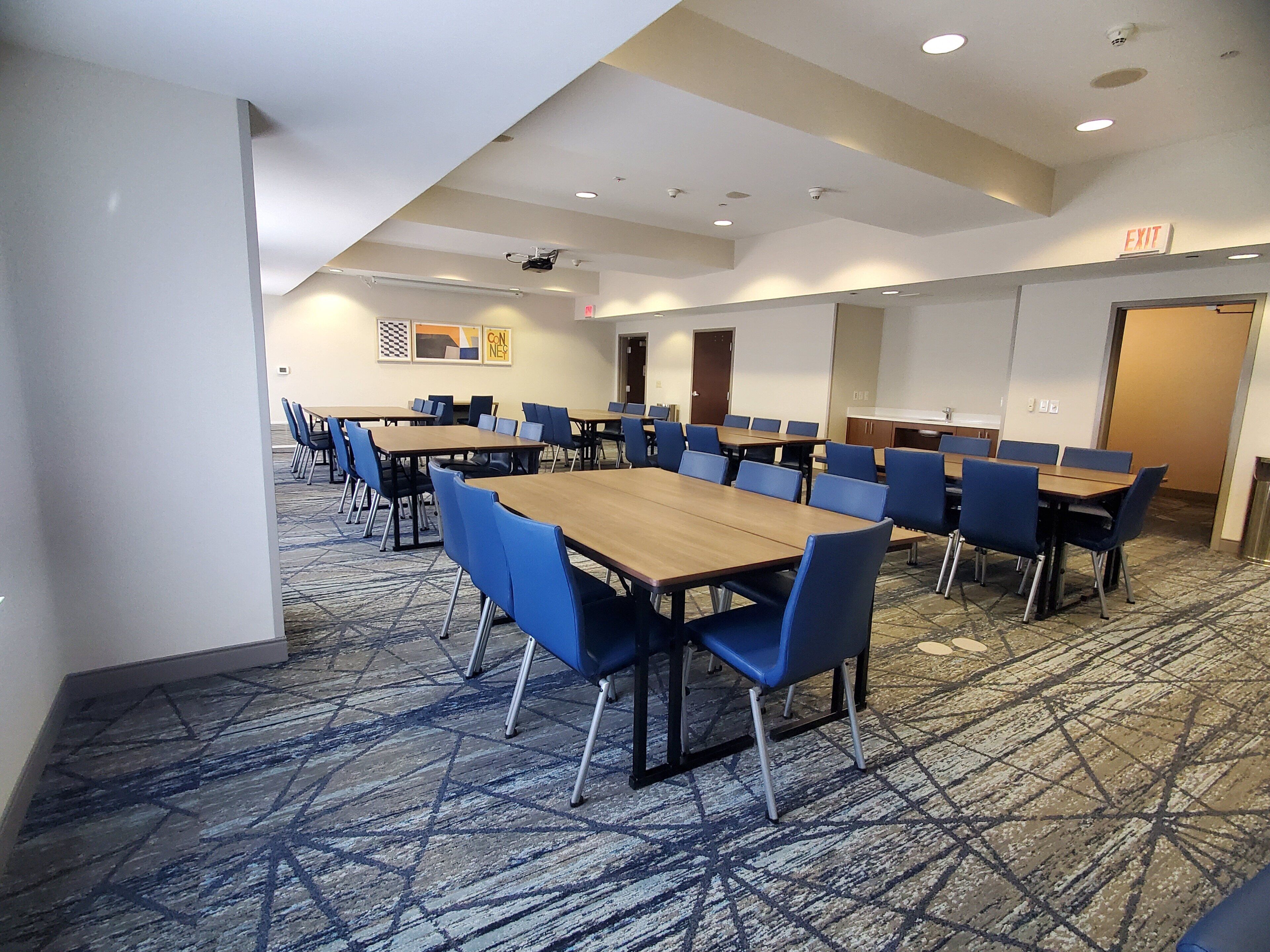 A conference room with multiple tables and blue chairs, carpeted floor, and ceiling lights.