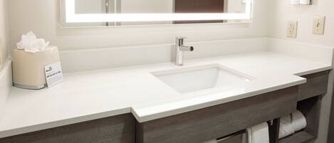 A bathroom with a white sink, a large mirror, a towel rack, and a tissue box.