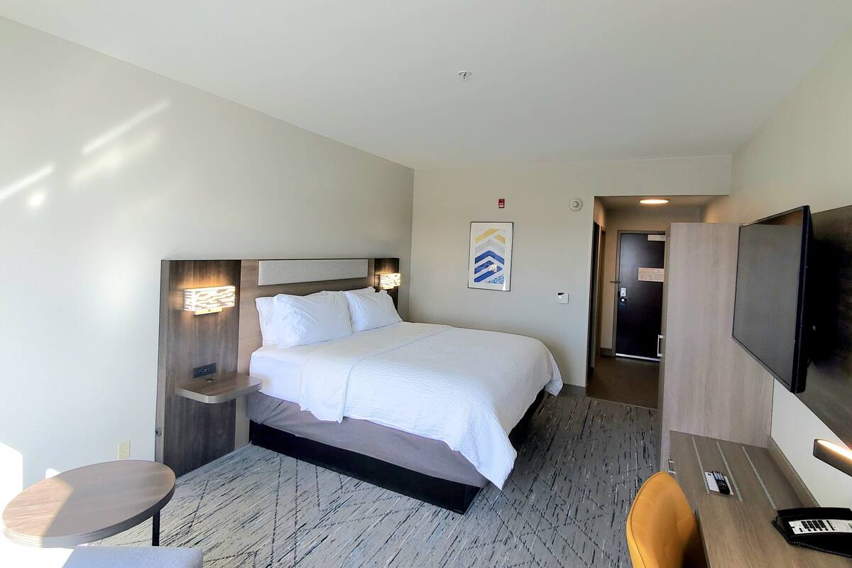 A modern hotel room with a bed, bedside table, chair, and a flat-screen TV.