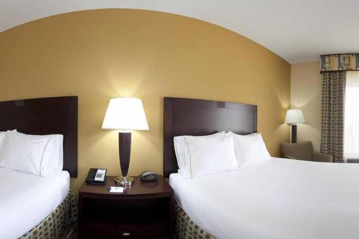 A hotel room with two beds, a curved wall, and a lamp between them.