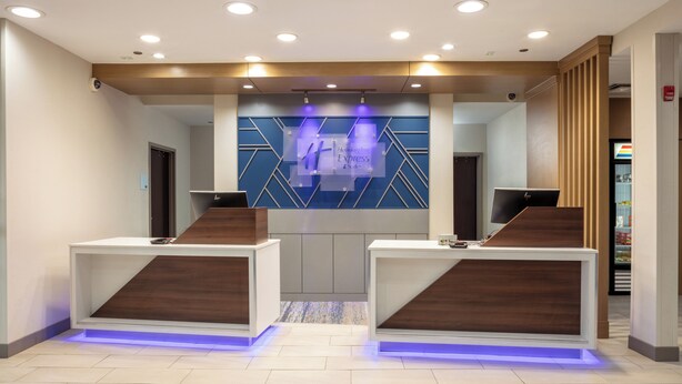 A reception area with two reception desks, a blue geometric wall design, and a visible fire alarm. - Holiday Inn Express & Suites El Paso West by IHG (El Paso)