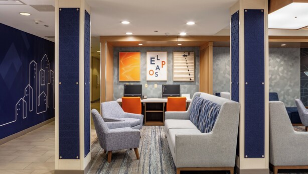A modern lounge area with a sofa, armchairs, and a desk with two monitors. - Holiday Inn Express & Suites El Paso West by IHG (El Paso)