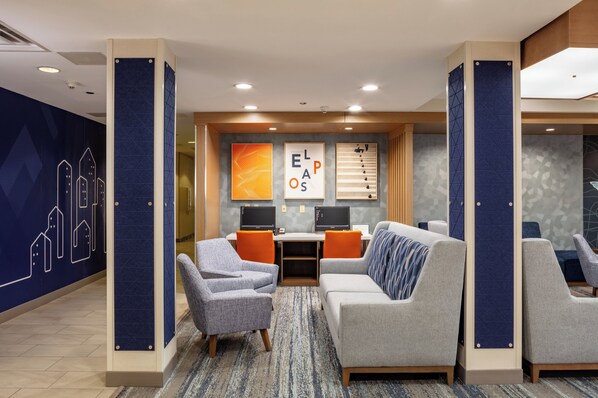 A modern lounge area with a sofa, armchairs, and a desk with two monitors. - Holiday Inn Express & Suites El Paso West by IHG (El Paso)
