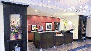 A reception area with a dark reception desk, a welcome sign, and a floral arrangement. - Hampton Inn Orange (Orange)