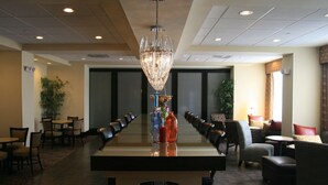 A conference room with a long table, chairs, a chandelier, and a plant. - Hampton Inn Orange (Orange)