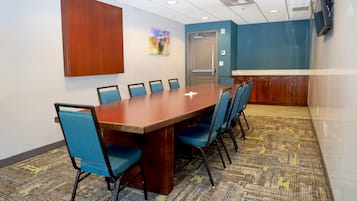 A conference room with a long table, blue chairs, a wooden cabinet, and a patterned carpet.