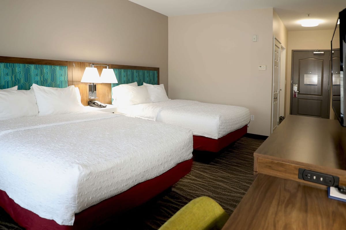 Ett hotellrum med två sängar, ett skrivbord, en stol, en lampa och en tv.