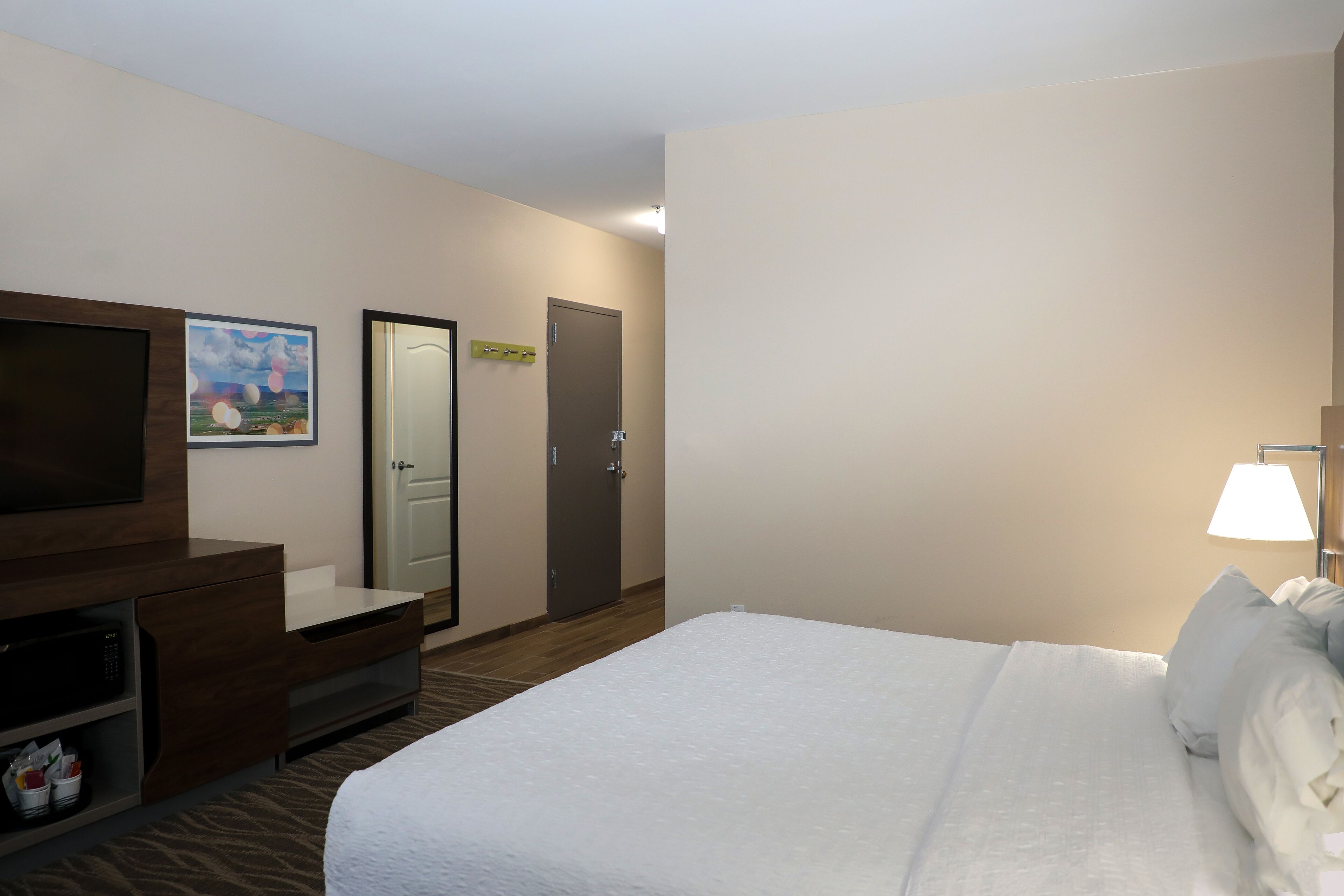 Quarto de hotel com uma cama, televisão, secretária e micro-ondas, e uma porta.