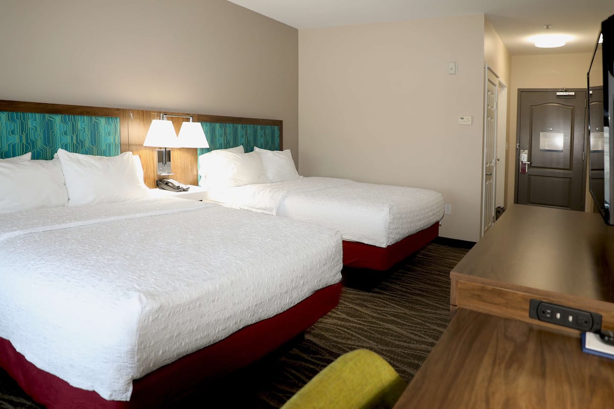 Ett hotellrum med två sängar, ett skrivbord, en stol, en lampa och en tv.