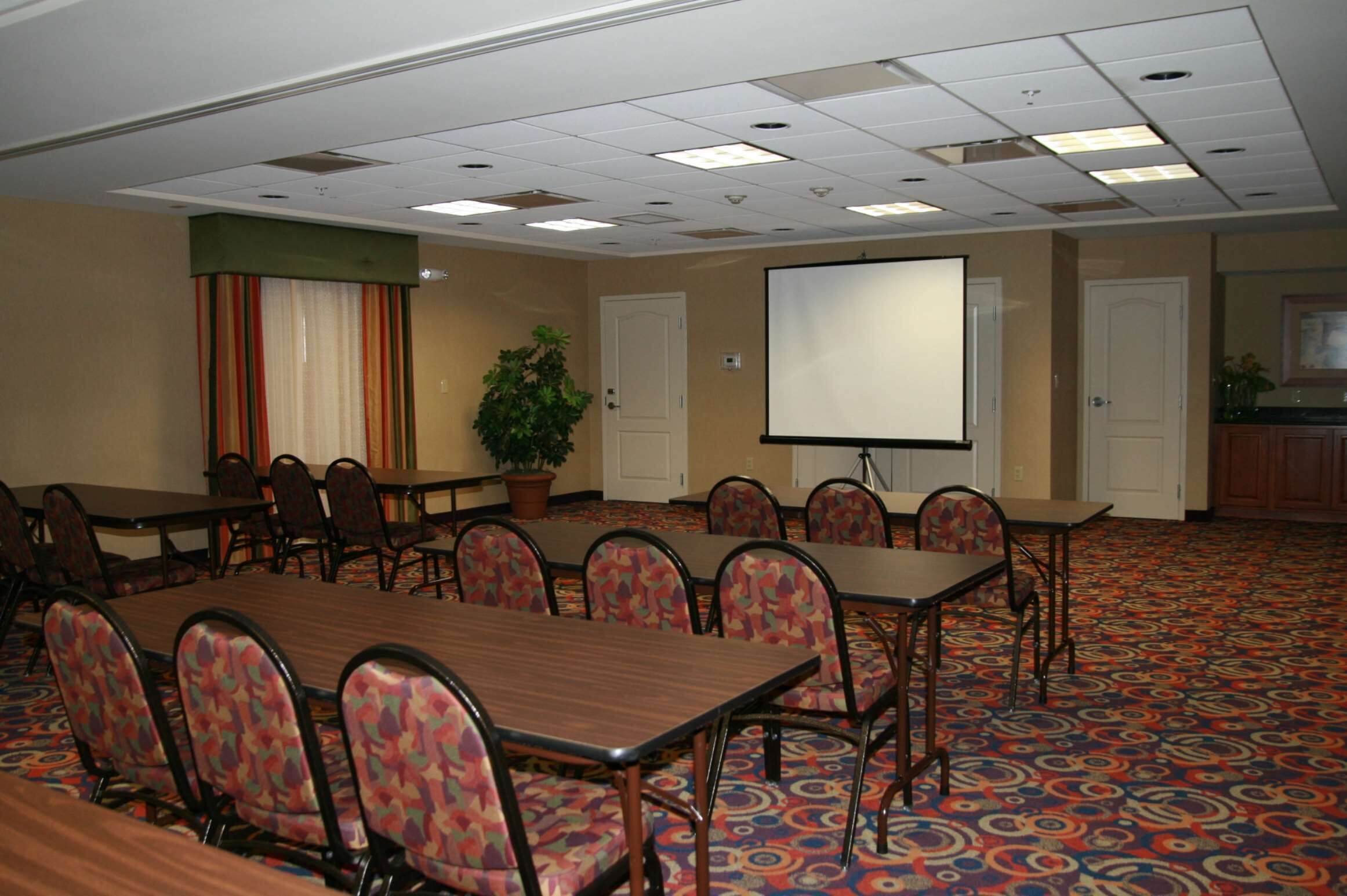 A conference room with a large table, multiple chairs, a projector screen, and a patterned carpet.