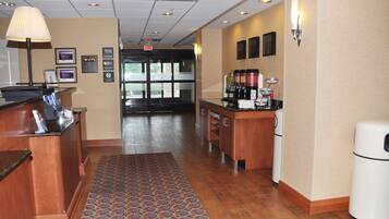 A hotel lobby with a reception desk, a coffee station, and a patterned rug.