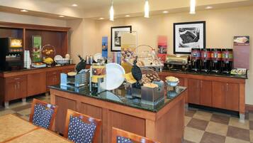 A hotel breakfast area with a central island, seating, and various breakfast items.
