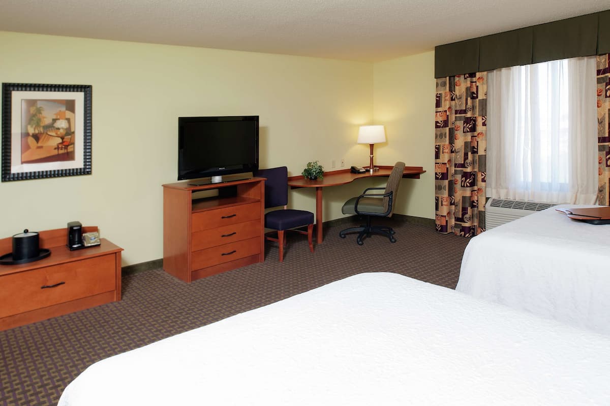 A hotel room with a bed, a desk with a computer, a television, a chair, and a small table with a lamp.