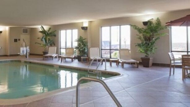 An indoor swimming pool with tiled flooring, lounge chairs, and potted plants.