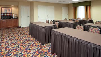 Un salón de conferencias con varias mesas y sillas, una estación de café y alfombra estampada.