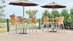 An outdoor patio with two tables and four chairs, each with a brown umbrella.