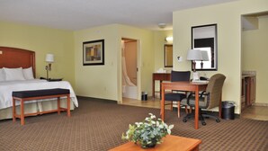 A hotel room with a bed, desk, chair, and a small table with a plant.