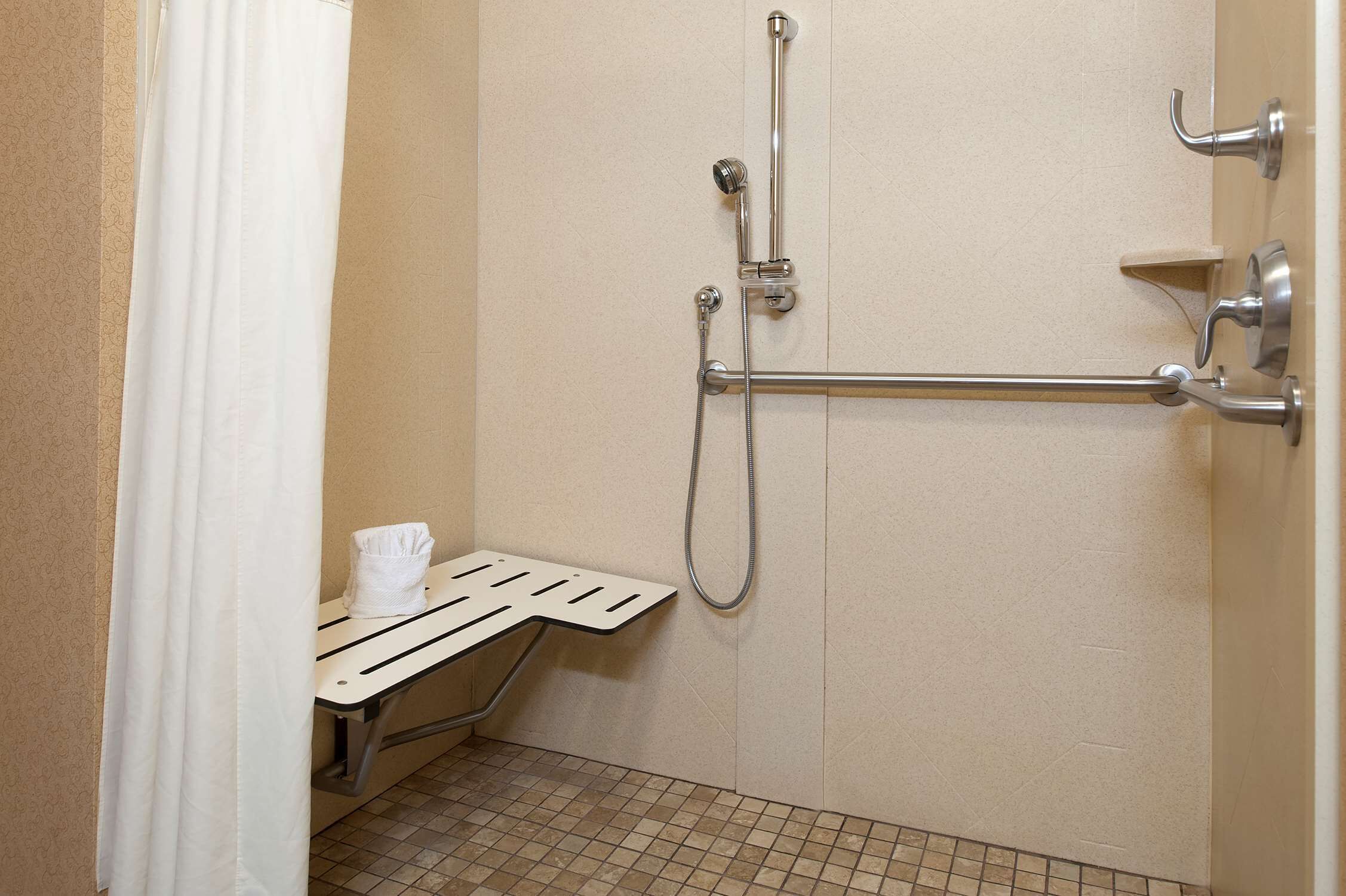 A shower area with a grab bar, a towel rack, and a bench.