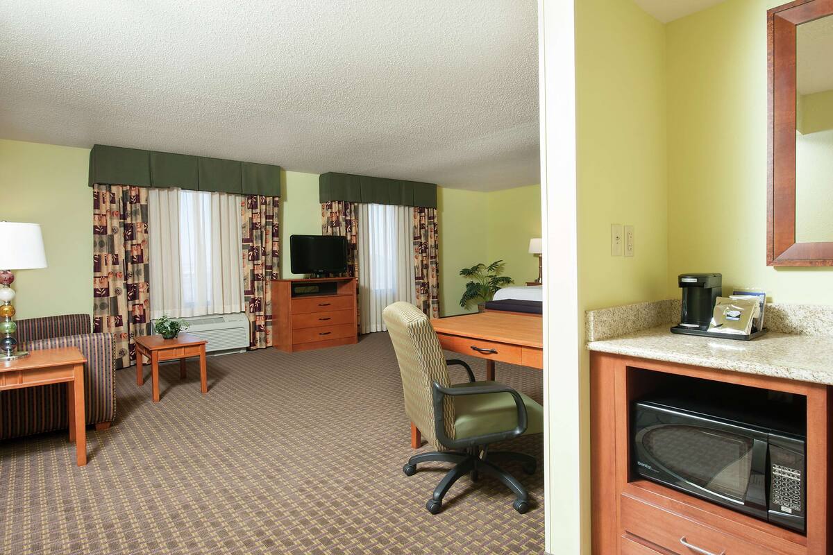 A hotel room with a sofa, a desk, a chair, a television, a coffee maker, and a microwave.