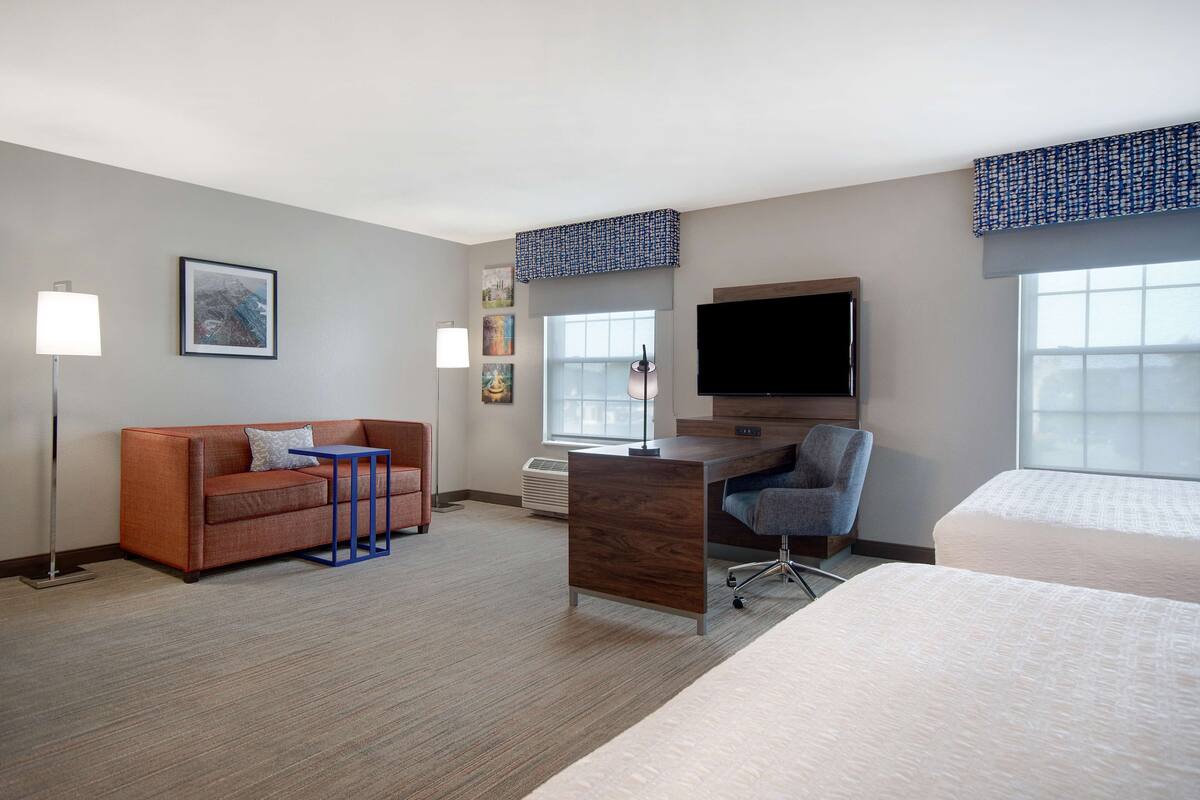 A hotel room with a sofa, desk, chair, TV, and two beds.