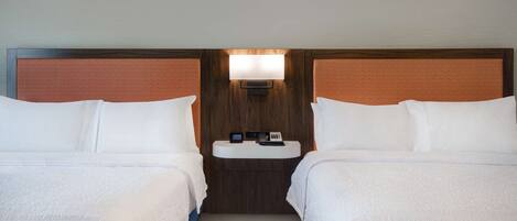 Habitación de hotel con dos camas, una mesita de noche con lámpara y una pequeña mesa.