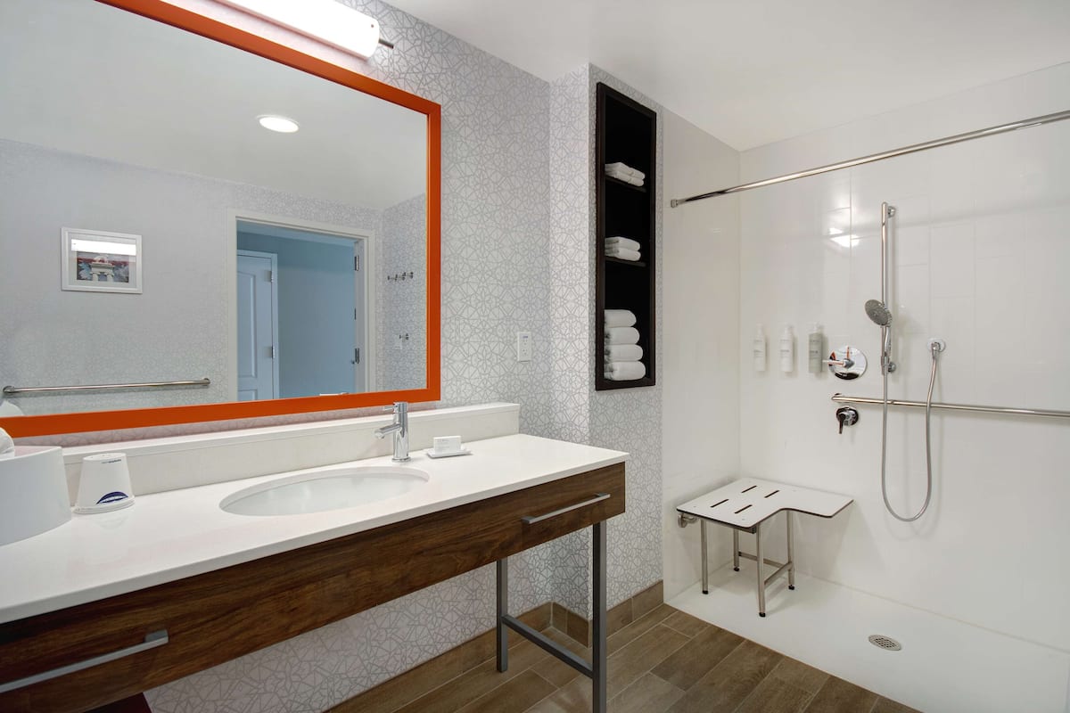 A modern bathroom with a large mirror, white sink, and shower area.
