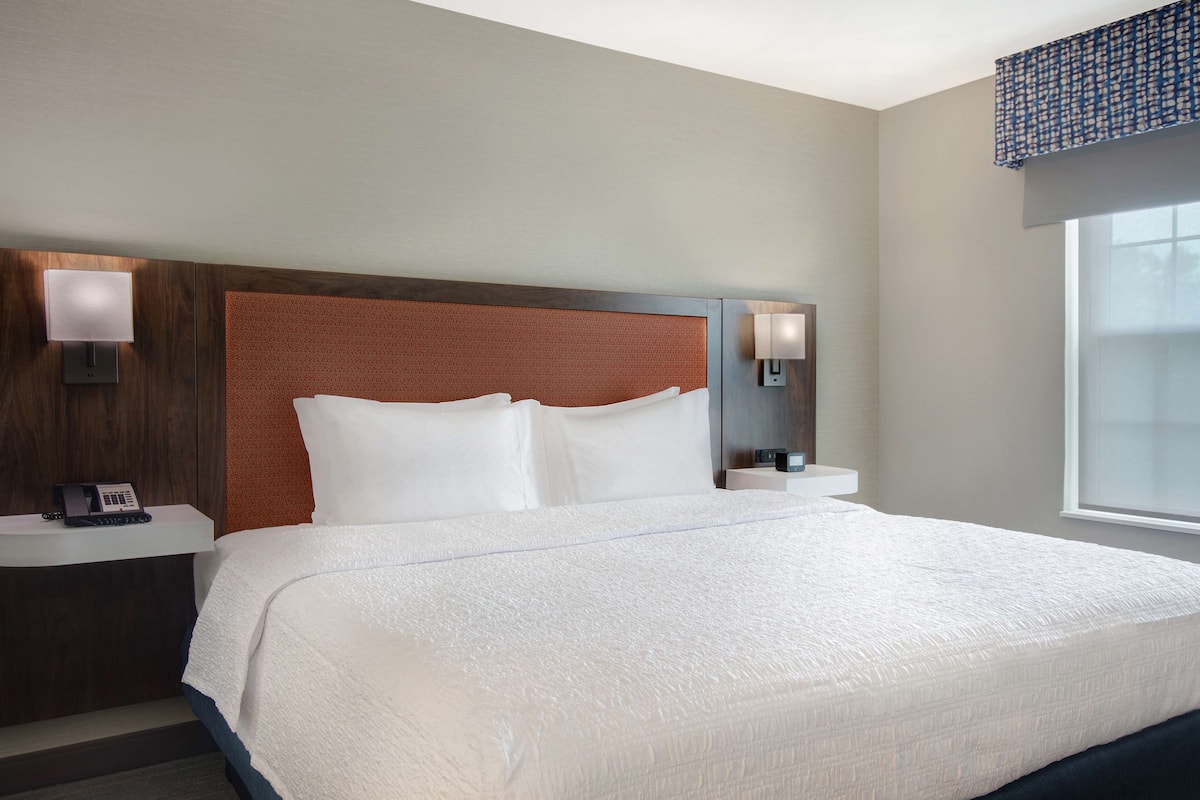 A hotel room with a large bed, two bedside tables, and a headboard with a textured design.
