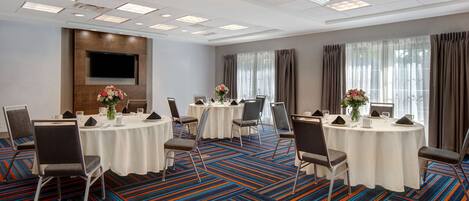 A conference room with round tables, chairs, and a flat-screen TV on the wall.